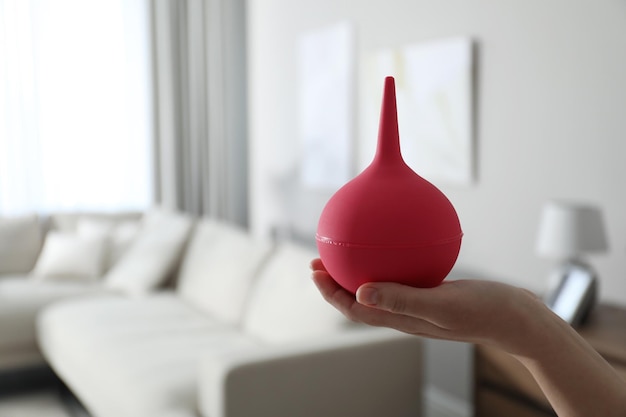 Woman holding pink enema at home closeup Space for text