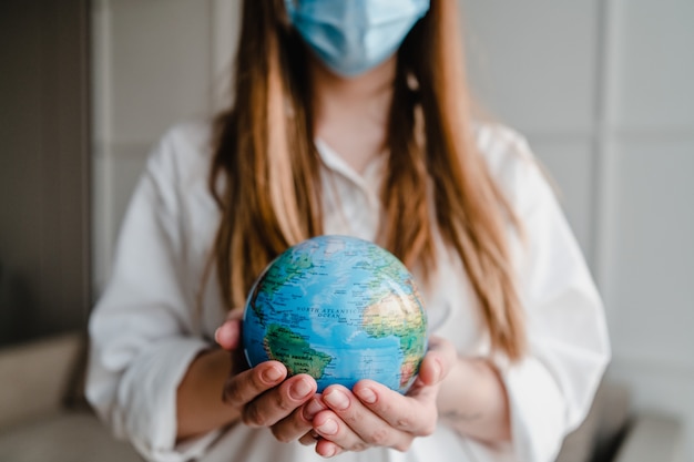 Woman holding planet earth globe at home wearing mask