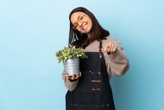 Photo woman holding a plant  pointing front with happy expression