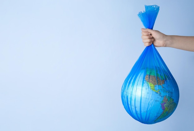 Woman holding plastic bag with globe and space for text on light background closeup Environmental conservation