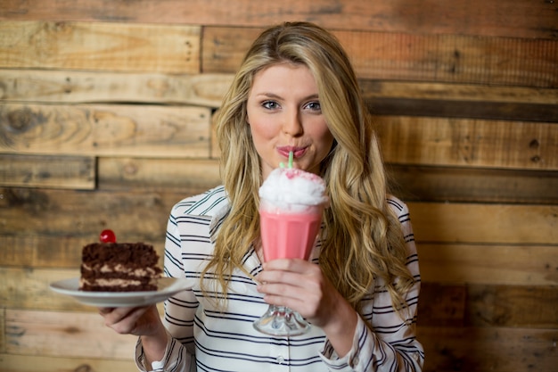 Woman holding plate of pastry and drinking milkshake with a straw