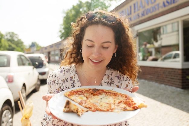 Photo a woman holding a plate of pizza in front of a restaurant.