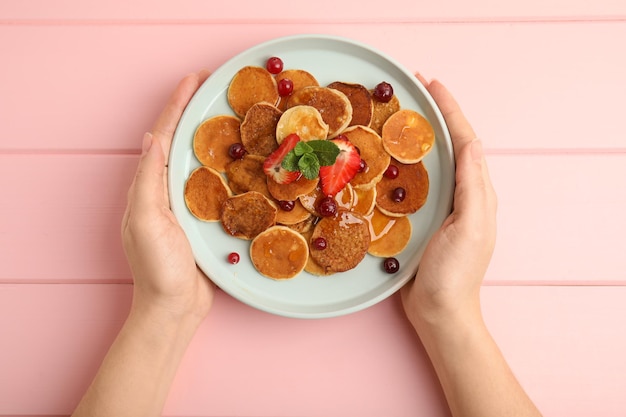 Woman holding plate with cereal pancakes at pink wooden table top view