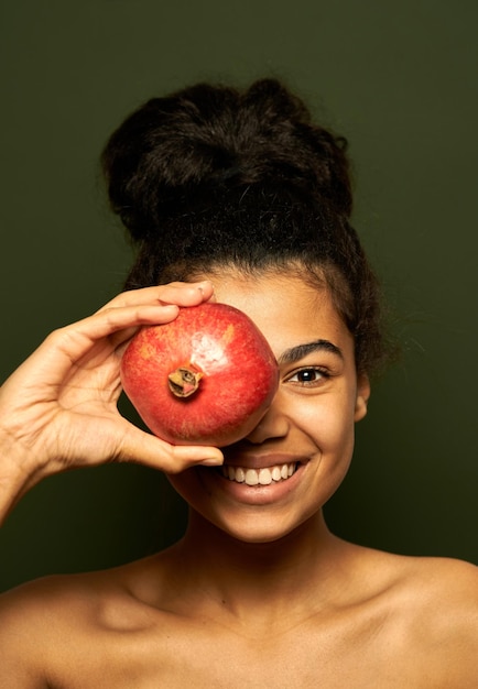 woman holding pomegranate fruit on her eye, posing isolated on green
