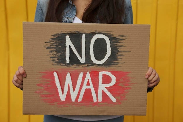 Woman holding poster No War near yellow fence closeup