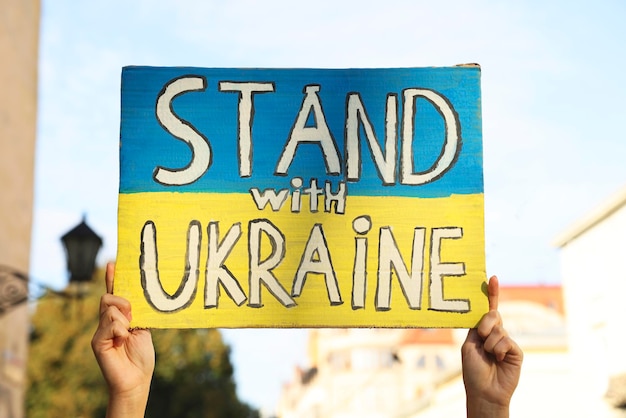 Woman holding poster Stand with Ukraine outdoors closeup