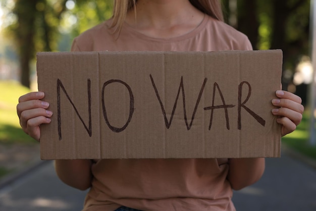 写真 公園のクローズ アップで戦争の言葉でポスターを保持している女性