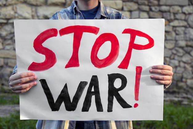 Woman holding poster with words Stop War against brick wall outdoors closeup