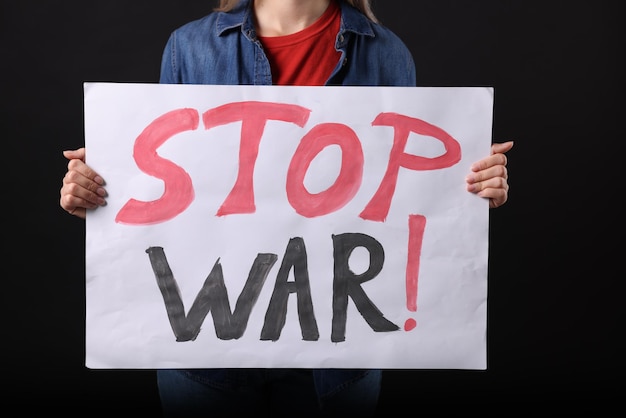 Woman holding poster with words Stop War on black background closeup