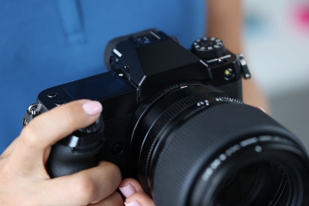 Photo woman holding professional black camera in hands and straightening lens closeup