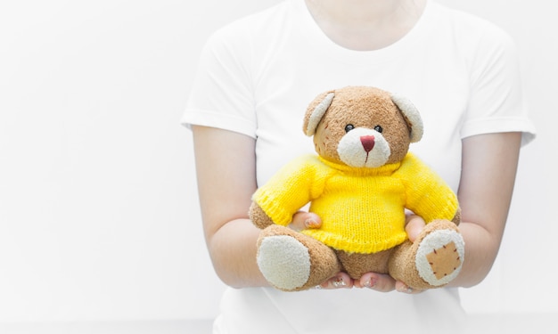 Woman holding and protecting give a brown Teddy Bear toy wear yellow shirts sitting on white background close-up,Symbol of love or dating