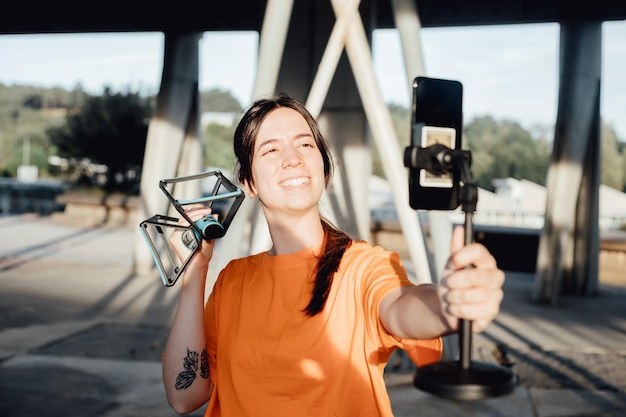 Woman holding push ups bar cross smiling at mobile phone\
describing the detailsspecifications and featuresexercise easy and\
cheapshooting a video and making photos to upload to websites and\
network