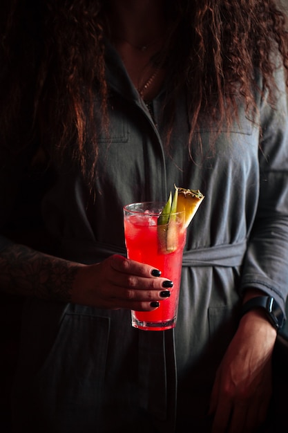 Woman holding red cocktail in a highball with ice and pineapple