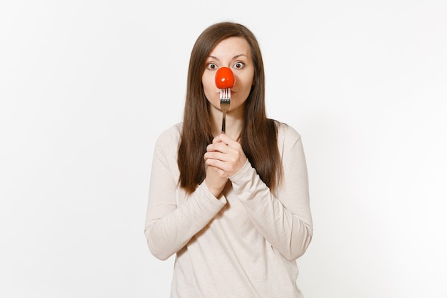 Woman holding red fresh tomato on fork in front nose like clown isolated on white background. Proper nutrition, vegetarian food, healthy lifestyle, vegetable concept. Advertising area with copy space.