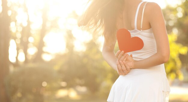 Woman holding a red heart behind the back. Close-up