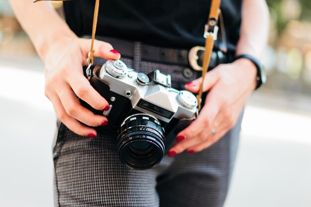 Woman holding a retro camera on the street. Hipster look. Crop photo