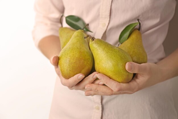 Woman holding ripe pears on light background closeup