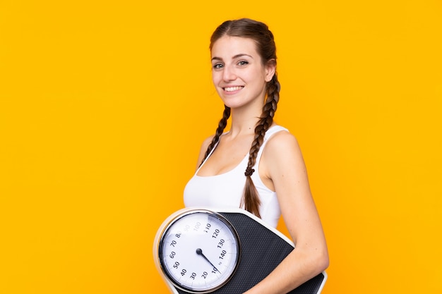 Woman holding a scale over yellow wall