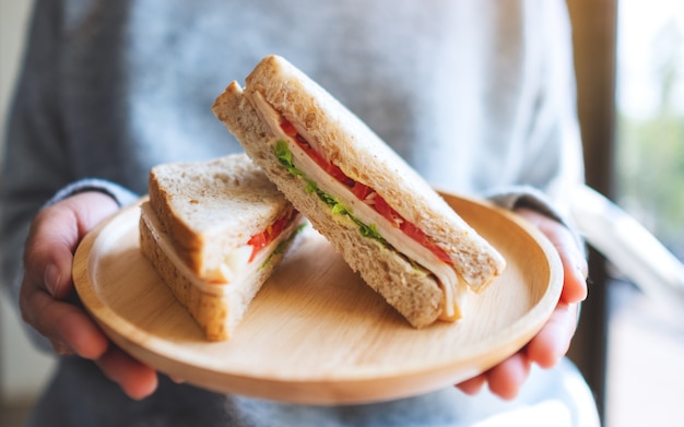 A woman holding and serving two pieces of whole wheat sandwich in wooden plate