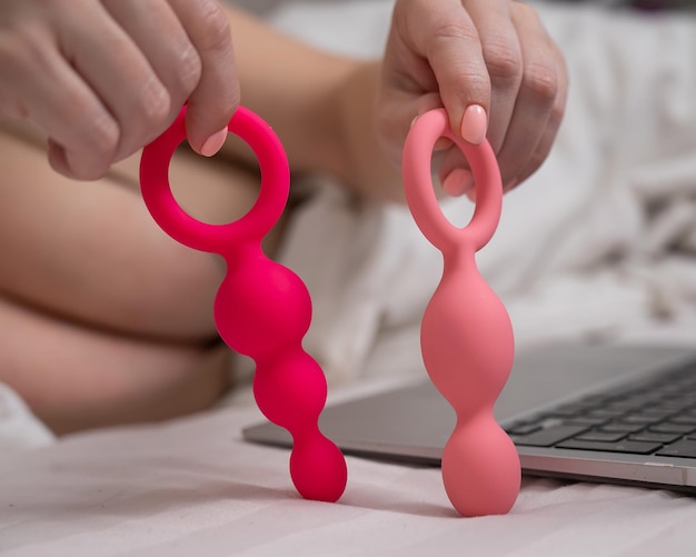 Woman holding a set of anal beads next to a laptop while lying in bed