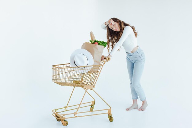 woman holding a shopping bag full of groceries, mango, salad, radish, lemon, carrots on white backgr