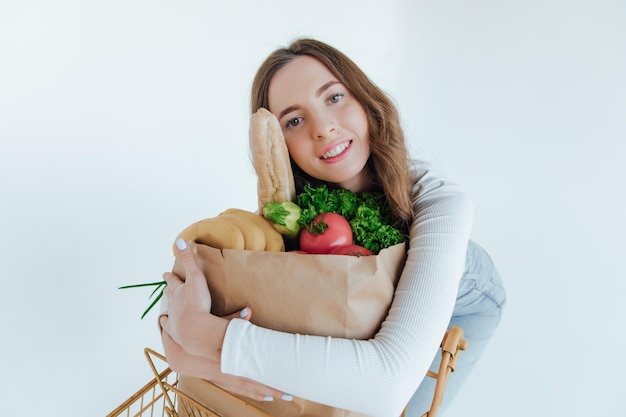 woman holding a shopping bag full of groceries, mango, salad, radish, lemon, carrots on white backgr