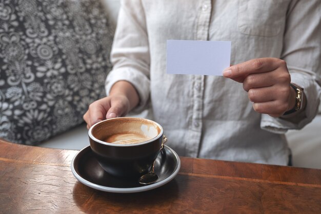 A woman holding and showing a blank empty business card to someone while drinking coffee