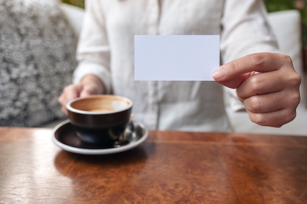 Una donna che tiene e che mostra un biglietto da visita vuoto in bianco a qualcuno mentre beve il caffè