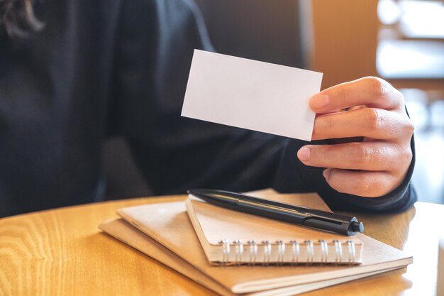 A woman holding and showing an empty business card with notebooks on table