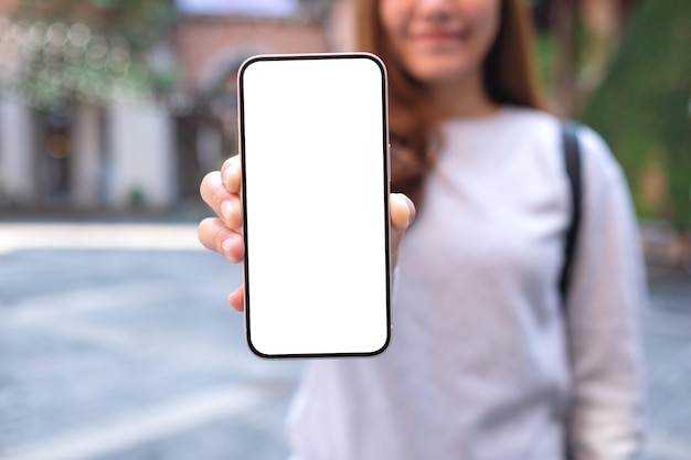 Woman holding and showing a mobile phone with blank white screen in the outdoors
