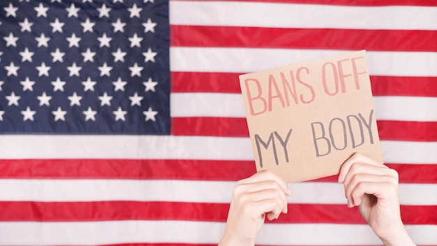 Woman holding a sign Bans Off My Body American flag on background Protest against anti abortion law