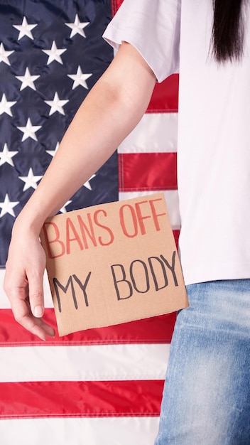 Woman holding sign Bans Off My Body American flag on background