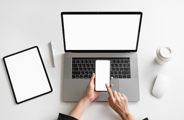 Woman holding smart phone, laptop and tablet on the table, mock up of blank screen. 