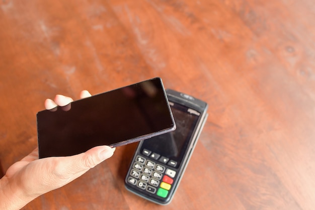 Woman holding smartphone close to electronic payment machine