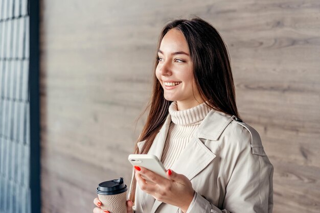 スマホとオフィスビルのフォルダーを持つ女性