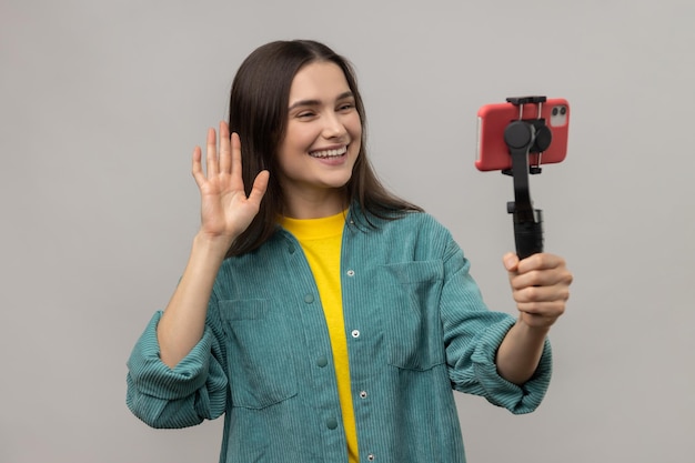 Woman holding smartphone on steadycam in hand blogger broadcasting livestream waving hand