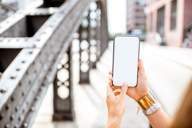 Woman holding smartphone with empty screen to copy paste on the iron bridge background