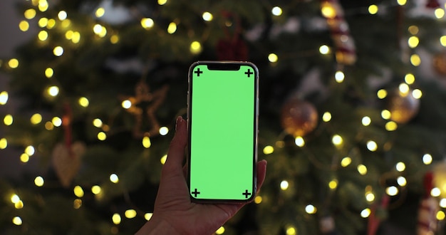 Woman holding smartphone with green screen on Christmas background Mobile phone with chroma key