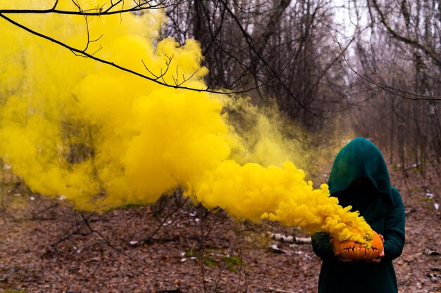 Woman holding smoke emitting pumpkin in forest