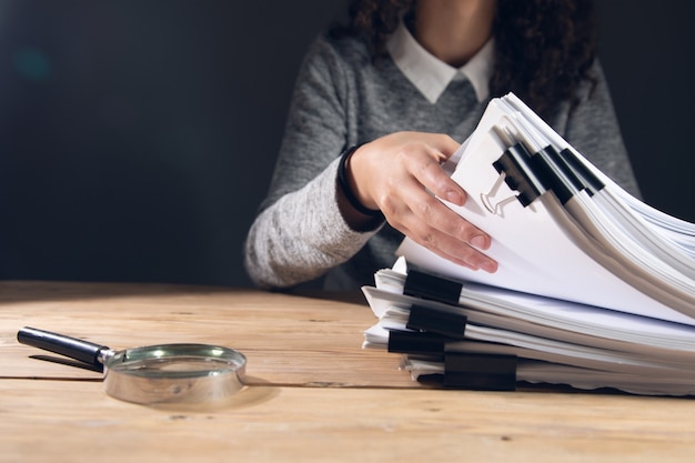 Photo woman holding stack of files with magnifier on the table