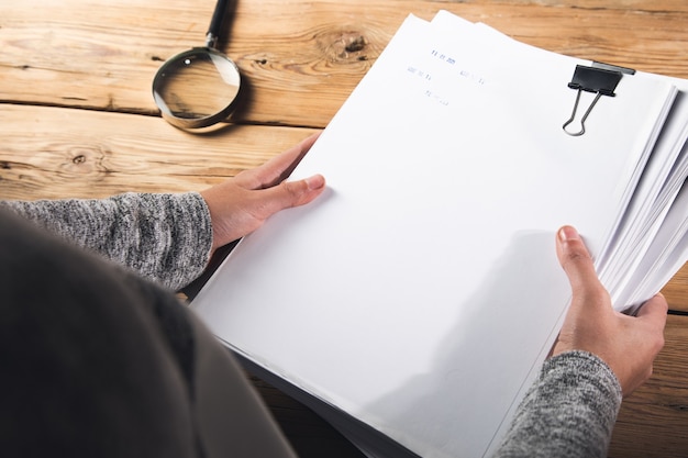 Woman holding stack of files with magnifier on the table