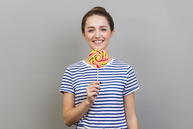 甘い菓子に夢中になっている彼女の手でスティックに縞模様のカラフルなロリポップを保持している女性