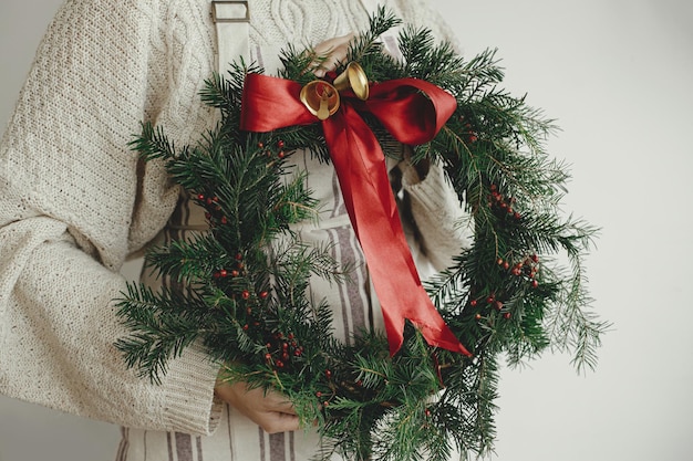 Woman holding stylish christmas wreath with red ribbon and golden bells Merry Christmas