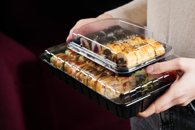 Photo woman holding sushi set box on black background