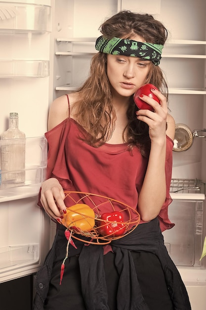 Woman holding sweet peppers at fridge