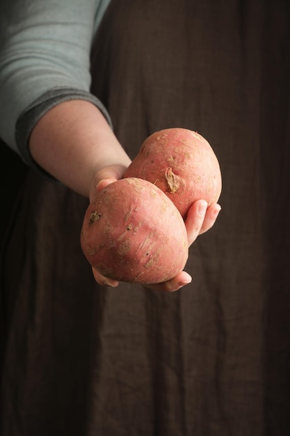 Woman holding sweet potatoes in hand Rustic style Vertical