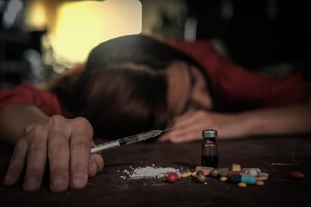 写真 テーブルの上で薬とボトルで注射器を握っている女性
