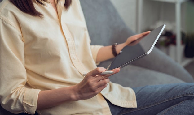 Photo woman holding a tablet and digital pen on the sofa in house.