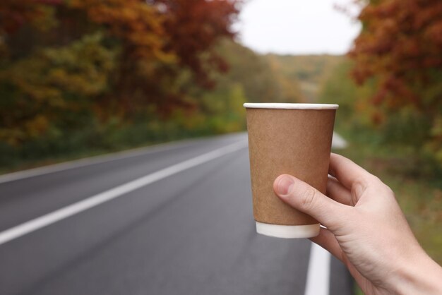 Photo woman holding takeaway cardboard coffee cup outdoors near road closeup autumn season