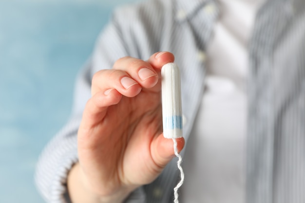 Woman holding tampon against blue surface